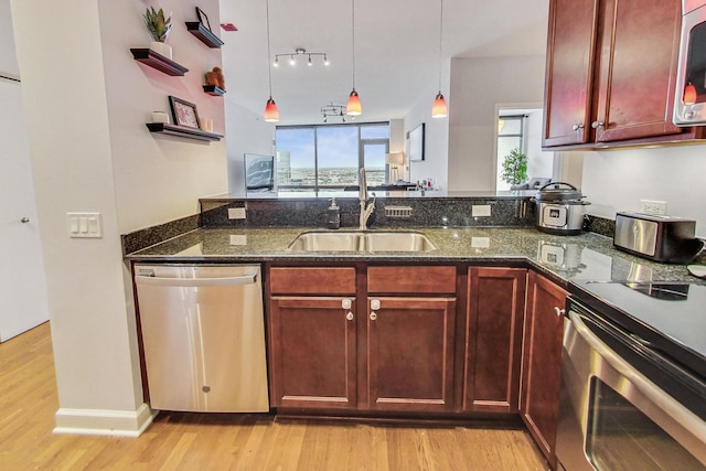 kitchen featuring light hardwood / wood-style flooring, hanging light fixtures, sink, dark stone countertops, and stainless steel appliances