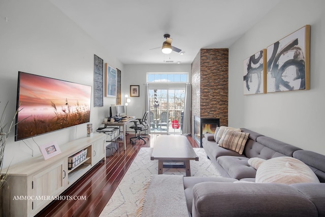 living room with a stone fireplace, dark wood-type flooring, and ceiling fan