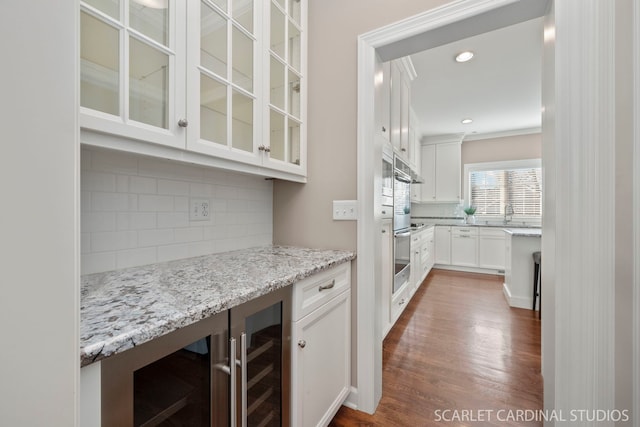 bar featuring beverage cooler, white cabinets, decorative backsplash, hardwood / wood-style flooring, and light stone counters