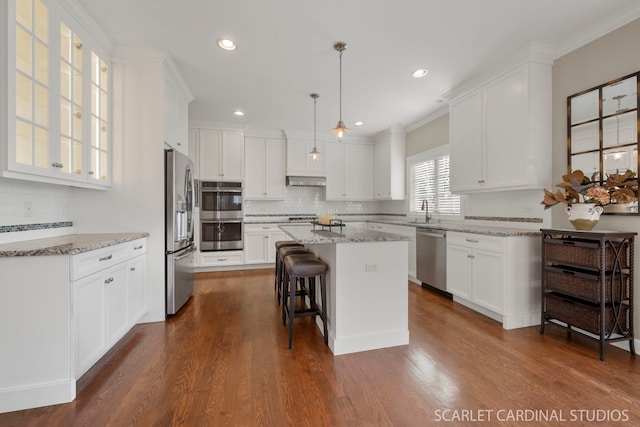 kitchen featuring light stone counters, decorative light fixtures, appliances with stainless steel finishes, a kitchen island, and white cabinets