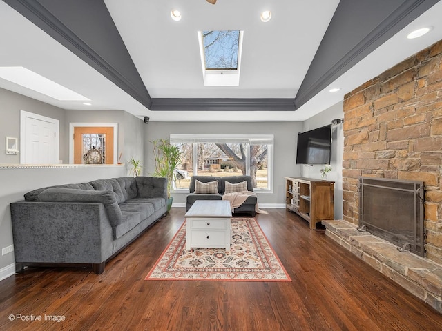 living room featuring lofted ceiling with skylight, ornamental molding, dark hardwood / wood-style flooring, a raised ceiling, and a fireplace