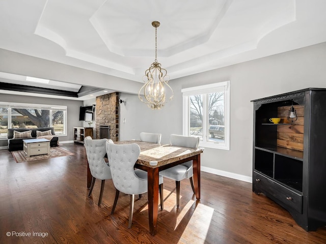 dining area featuring a fireplace, a tray ceiling, dark hardwood / wood-style flooring, and a notable chandelier