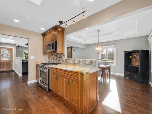 kitchen featuring pendant lighting, appliances with stainless steel finishes, a tray ceiling, light stone countertops, and decorative backsplash