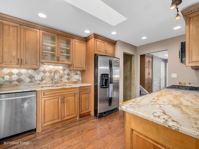 kitchen featuring sink, light stone counters, appliances with stainless steel finishes, hardwood / wood-style floors, and decorative backsplash