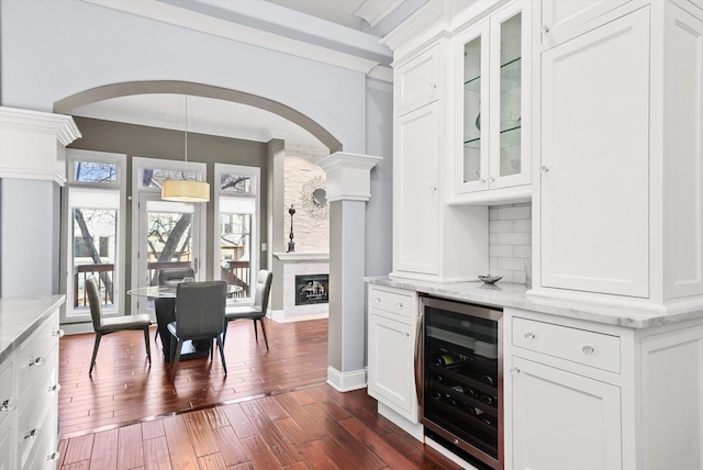 kitchen with white cabinets, beverage cooler, decorative backsplash, light stone countertops, and dark wood-type flooring