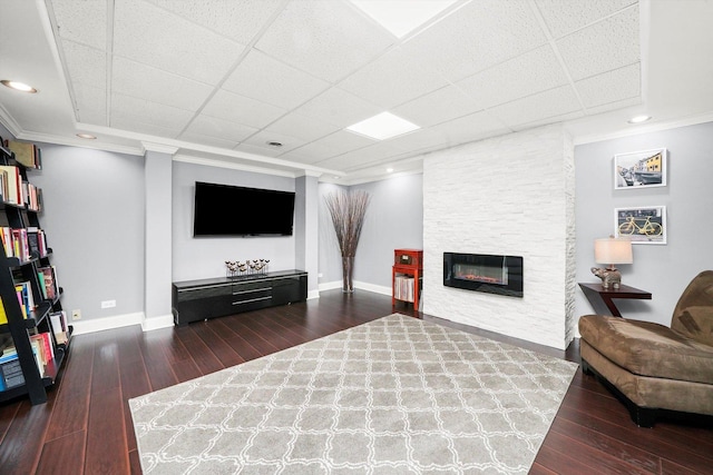 living room with ornamental molding, dark hardwood / wood-style floors, a drop ceiling, and a fireplace