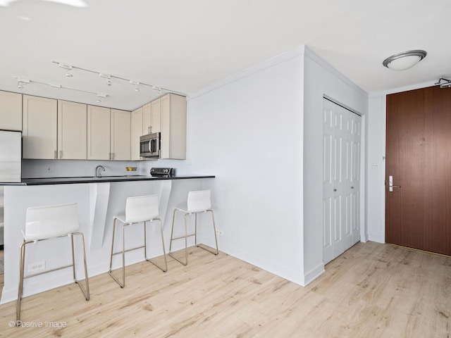 kitchen with crown molding, light wood-type flooring, cream cabinets, a kitchen bar, and rail lighting