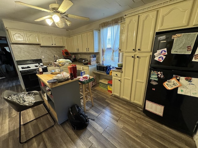 kitchen featuring black refrigerator, cream cabinetry, gas range oven, and dark hardwood / wood-style flooring