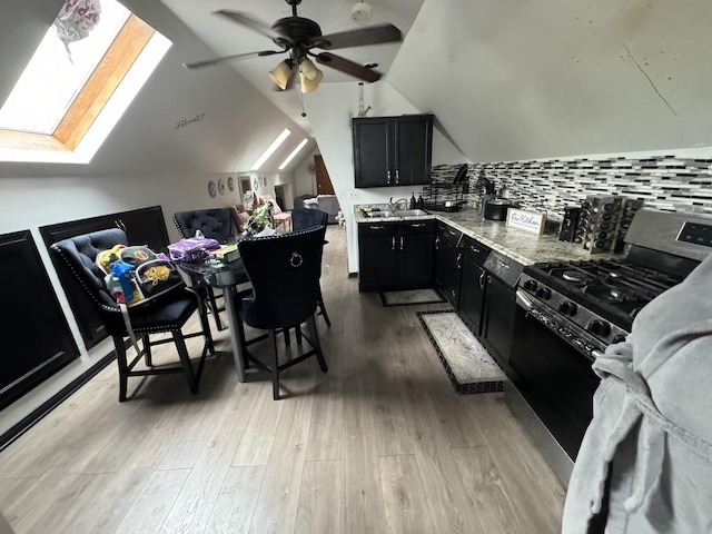 kitchen featuring stainless steel range with gas stovetop, sink, tasteful backsplash, light stone countertops, and vaulted ceiling with skylight