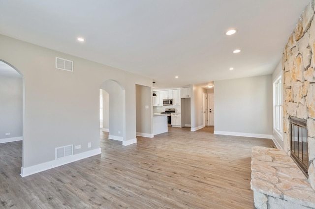 unfurnished living room with light hardwood / wood-style flooring and a stone fireplace