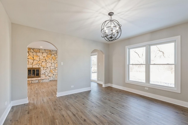 unfurnished living room with wood-type flooring, a chandelier, and a stone fireplace