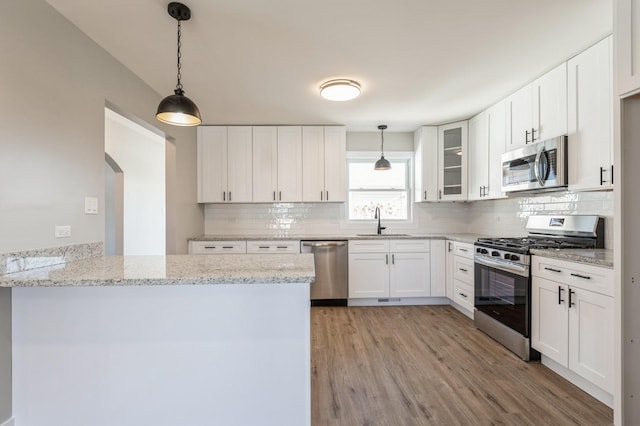 kitchen with light stone countertops, white cabinets, sink, kitchen peninsula, and stainless steel appliances