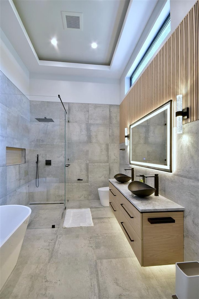 full bathroom featuring separate shower and tub, tile walls, a tray ceiling, toilet, and vanity