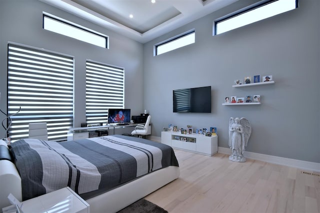 bedroom featuring light hardwood / wood-style floors, a high ceiling, and a raised ceiling