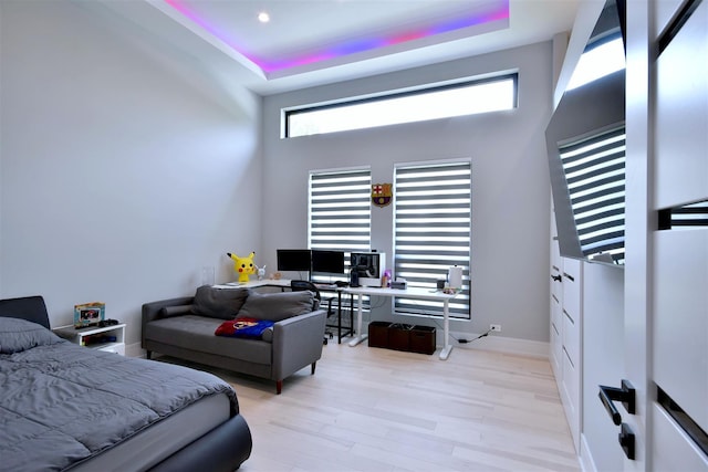 bedroom with a high ceiling, light hardwood / wood-style floors, and a tray ceiling