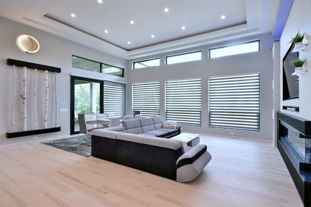 living room featuring light hardwood / wood-style flooring, a high ceiling, and a tray ceiling