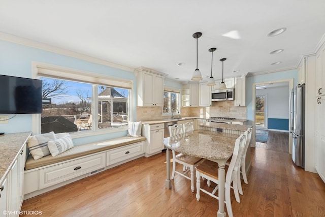 kitchen featuring white cabinetry, stainless steel appliances, tasteful backsplash, light stone countertops, and decorative light fixtures