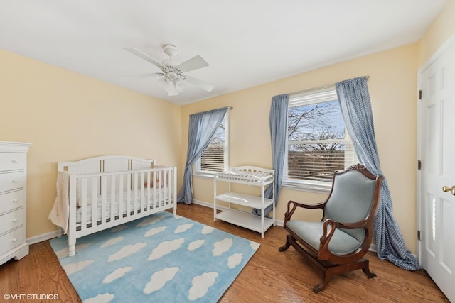 bedroom featuring hardwood / wood-style flooring, a crib, and ceiling fan