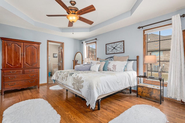 bedroom featuring hardwood / wood-style flooring, multiple windows, ceiling fan, and a raised ceiling