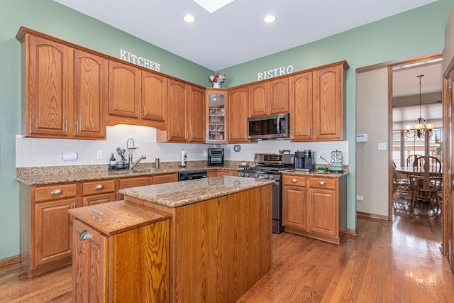 kitchen featuring sink, light stone countertops, a kitchen island, an inviting chandelier, and stainless steel appliances