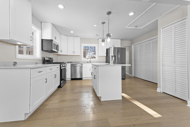 kitchen featuring white cabinetry, decorative light fixtures, light hardwood / wood-style flooring, a kitchen island, and stainless steel appliances