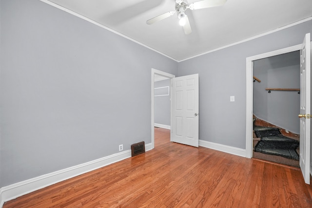 unfurnished bedroom with ceiling fan, ornamental molding, light hardwood / wood-style floors, a walk in closet, and a closet