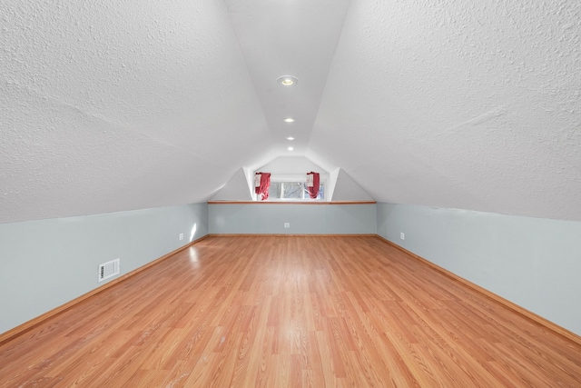 additional living space featuring lofted ceiling, a textured ceiling, and light hardwood / wood-style floors