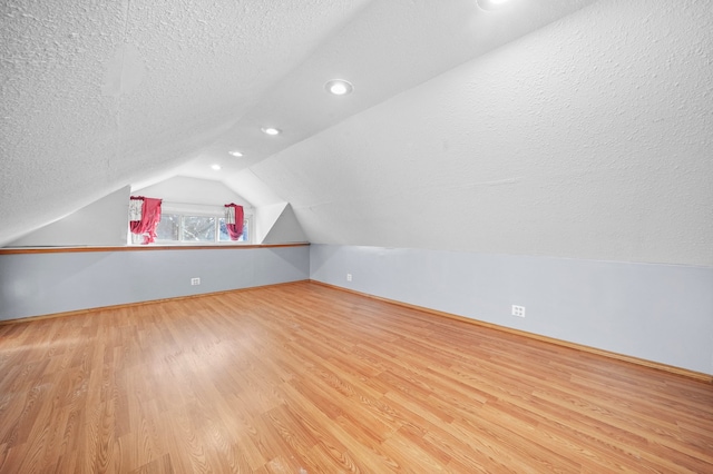 additional living space featuring lofted ceiling, light hardwood / wood-style flooring, and a textured ceiling