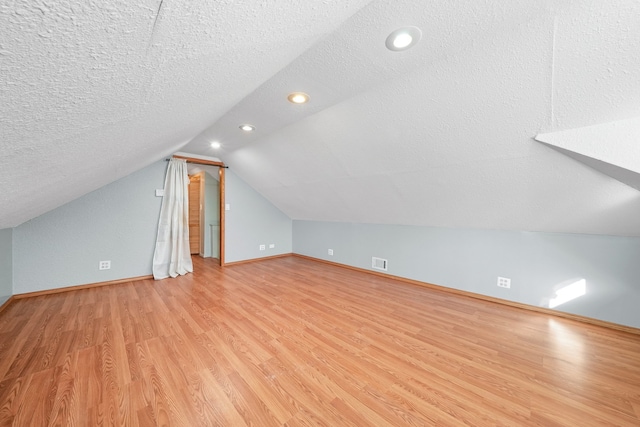 bonus room with light hardwood / wood-style floors, vaulted ceiling, and a textured ceiling