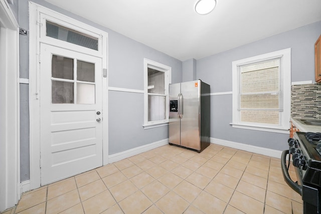 kitchen featuring black gas range, light tile patterned floors, backsplash, and stainless steel fridge