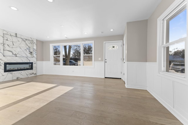 unfurnished living room with a high end fireplace, a healthy amount of sunlight, and light wood-type flooring