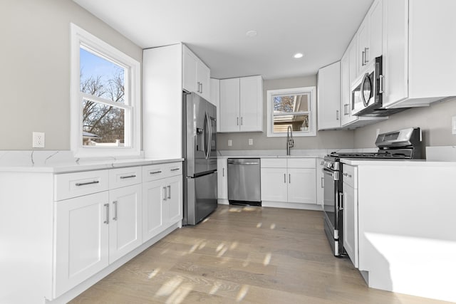 kitchen with sink, stainless steel appliances, white cabinets, and light wood-type flooring