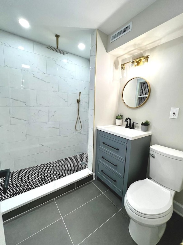 bathroom with vanity, toilet, a tile shower, and tile patterned flooring