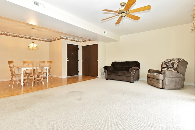 living area featuring ceiling fan with notable chandelier and carpet