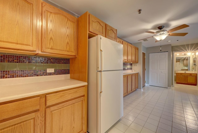 kitchen with white fridge, decorative backsplash, light brown cabinetry, light tile patterned flooring, and ceiling fan