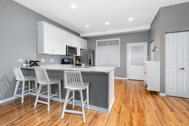 kitchen featuring a kitchen bar, sink, white cabinetry, kitchen peninsula, and stainless steel appliances