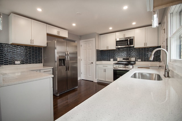 kitchen featuring appliances with stainless steel finishes, white cabinets, sink, pendant lighting, and light stone counters