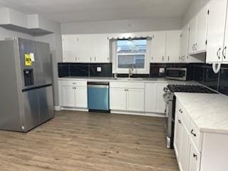 kitchen with stainless steel appliances, sink, light hardwood / wood-style flooring, and white cabinets