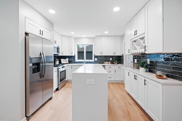 kitchen with a kitchen island, light hardwood / wood-style floors, white cabinetry, and appliances with stainless steel finishes