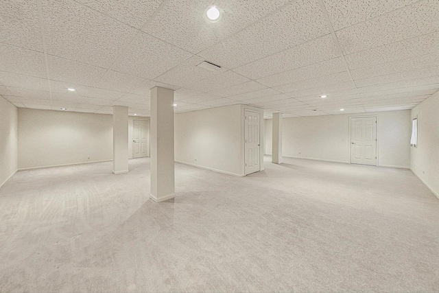 basement with a paneled ceiling and light carpet