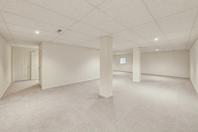 basement with a paneled ceiling and light carpet