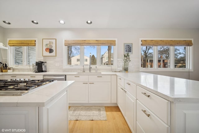 kitchen featuring sink, white cabinetry, backsplash, light hardwood / wood-style floors, and stainless steel gas stovetop