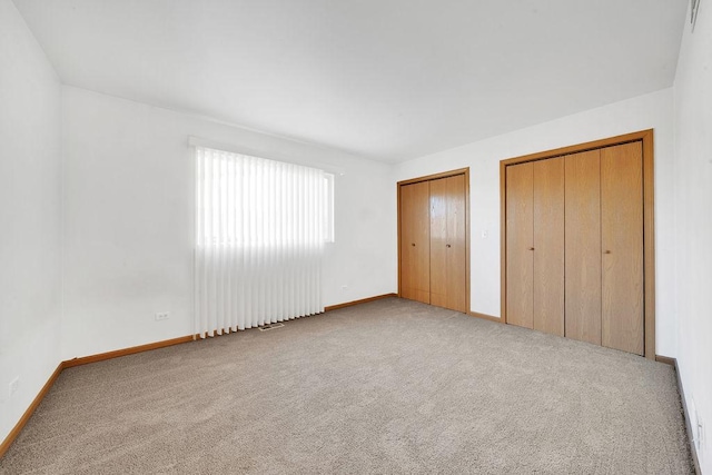 unfurnished bedroom with light carpet and two closets