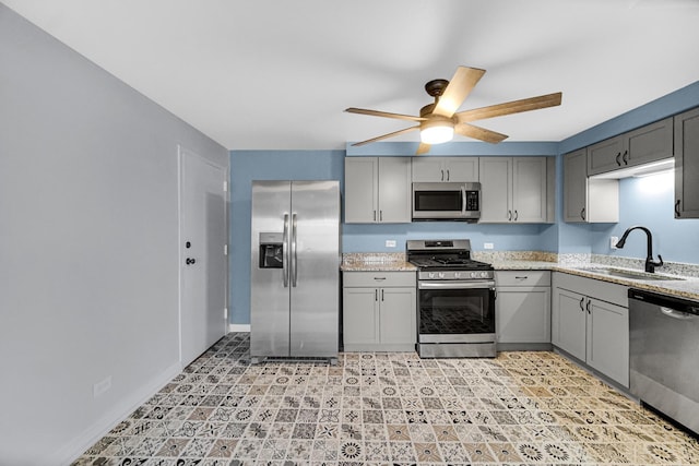 kitchen featuring ceiling fan, light stone countertops, gray cabinetry, sink, and stainless steel appliances