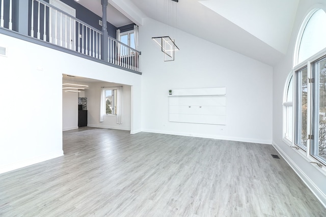 unfurnished living room with light wood-type flooring and high vaulted ceiling