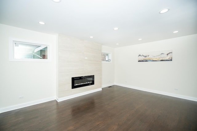 unfurnished living room with a tiled fireplace and dark wood-type flooring