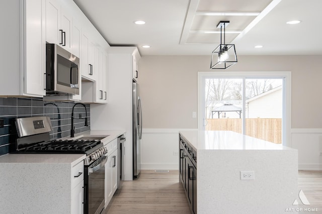 kitchen with backsplash, white cabinets, hanging light fixtures, and stainless steel appliances