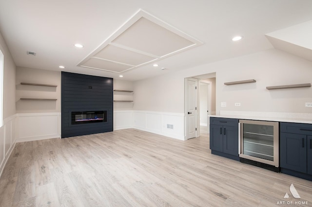 unfurnished living room featuring indoor bar, light wood-type flooring, beverage cooler, and a large fireplace