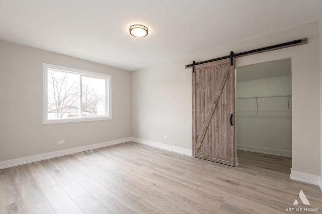 unfurnished bedroom featuring light wood-type flooring, a closet, a spacious closet, and a barn door