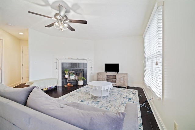 living room featuring ceiling fan, plenty of natural light, a tile fireplace, and wood-type flooring